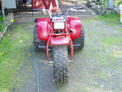 2000 Ford E350 - A red three-wheeled ATV is parked on a gravel and grass surface.