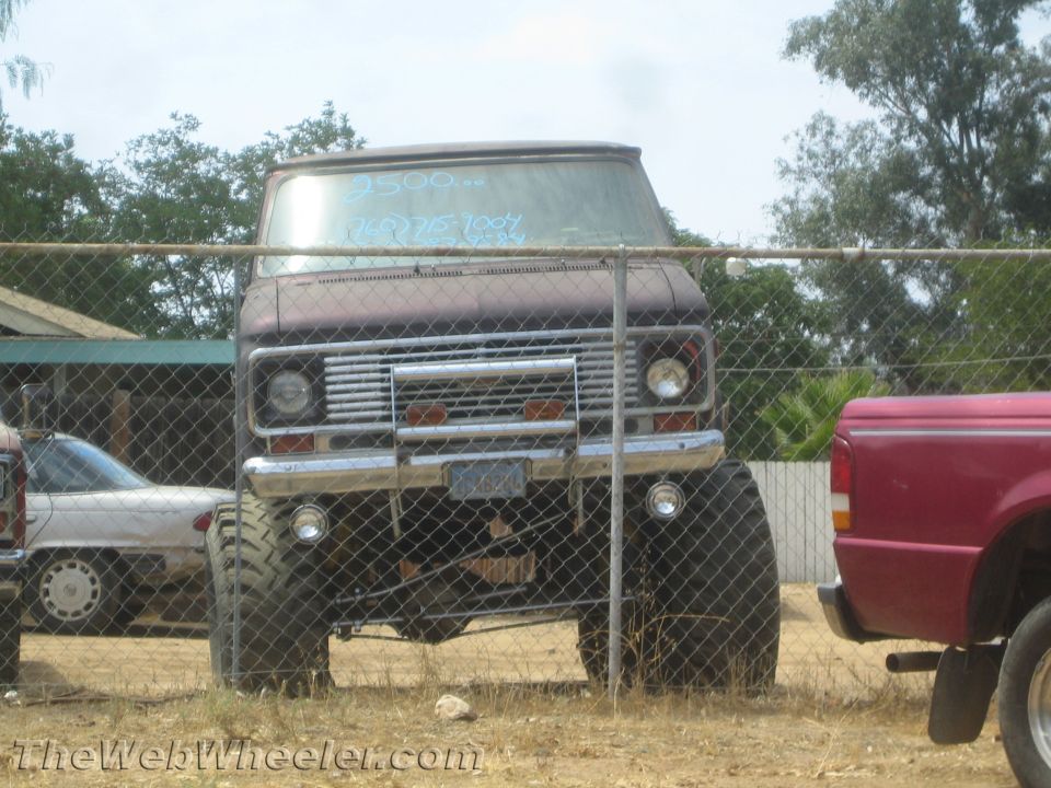 Maroon lifted Ford van on big tires with '2500' price on windshield, behind chain-link fence