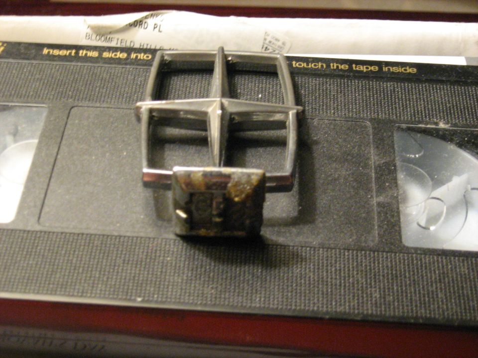 Chrome four-point star hood ornament with corroded base resting on a VHS cassette