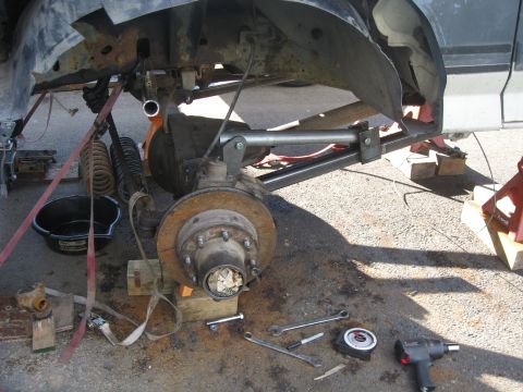 1990 Ford F-250 - The front suspension of a truck is undergoing repair, with various components and tools laid out on the ground.