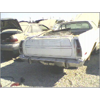 1973 Ford Ranchero - A white 1973 Ford Ranchero is seen from the rear in a junkyard, with other vehicles in the background.