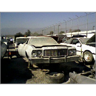 1973 Ford Ranchero - A 1973 Ford Ranchero sits in a junkyard, showing its front grille and headlights.