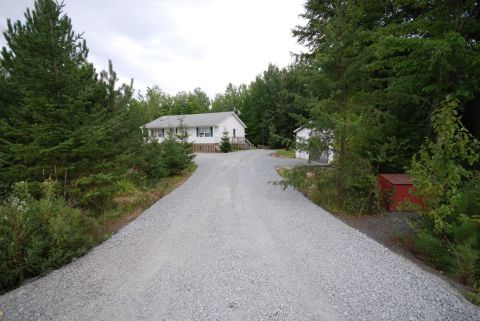 1996 Ford Bronco - A long gravel driveway winds through a wooded area towards a modest white house and a small outbuilding.