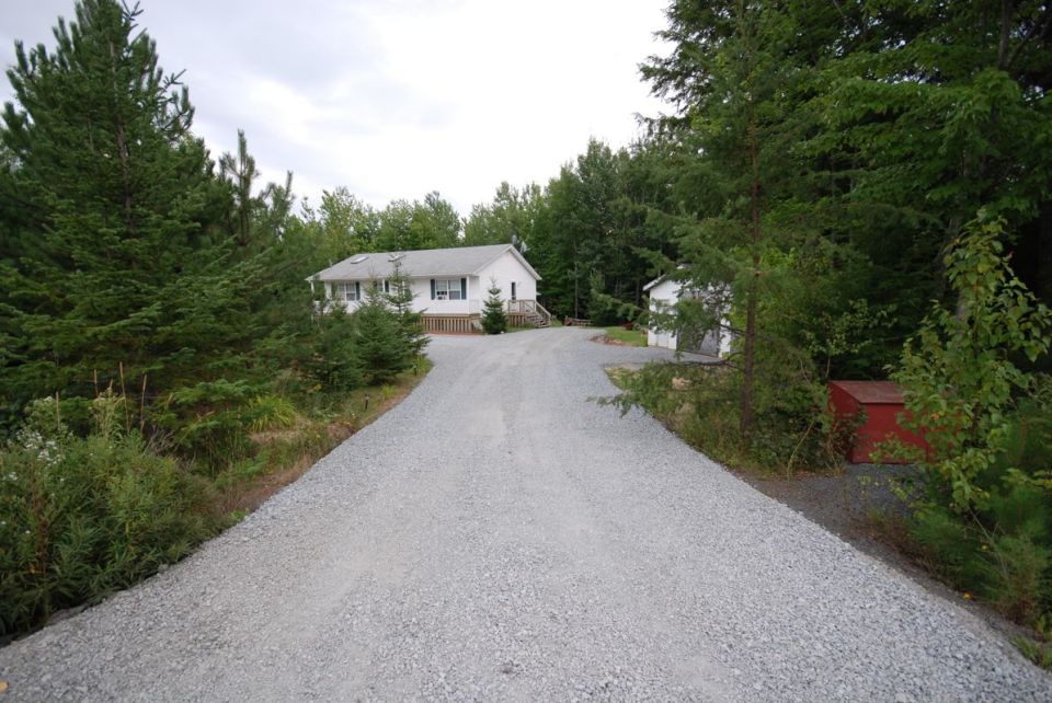 Gravel driveway leading to a white house with a red storage shed to the right