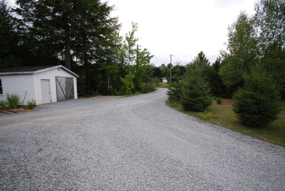 Gravel driveway leading to a white shed, surrounded by trees