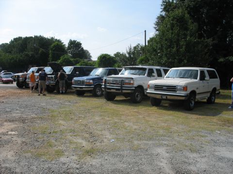 1995 Ford C-350 (Centurion Conversions) - Several Ford trucks and Broncos are parked in a gravel lot under a clear sky.