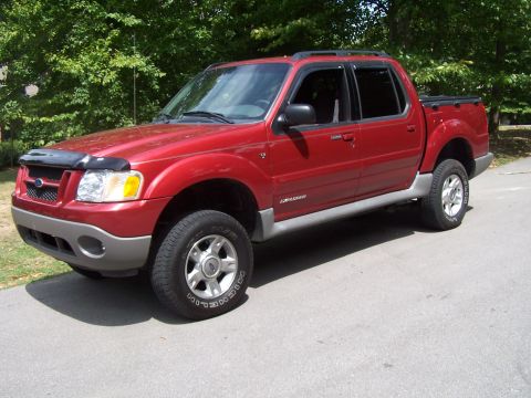 2002 Ford Sport Trac - Red 2002 Ford Sport Trac pickup truck parked on asphalt with trees in background.