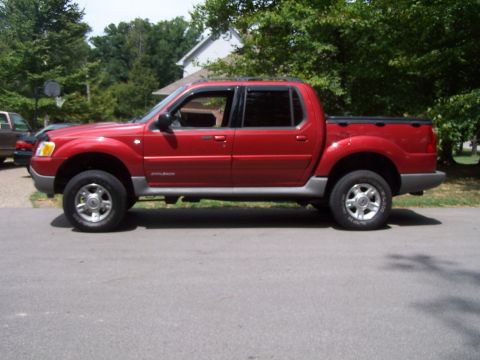 2002 Ford Sport Trac - This red Ford Sport Trac is shown from the side, parked on a paved surface with trees and a house in the background.