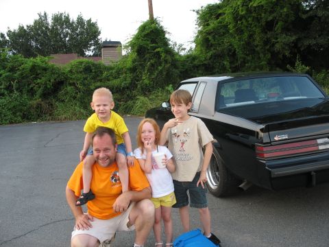1995 Ford C-350 (Centurion Conversions) - A family of four poses for a photo with a black car in the background.