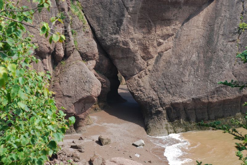 Large rock formations with a narrow opening leading to a beach and water