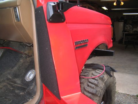 1989 Ford Bronco - Close-up view of the interior and exterior of a red Ford Bronco, highlighting the door panel and fender emblem.