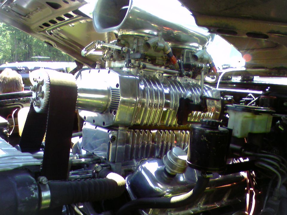 Polished roots supercharger with dual carbs, chrome scoop and toothed drive belt in an open engine bay
