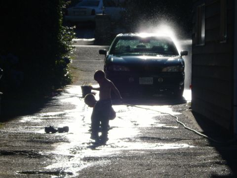 1989 Ford Bronco - Kids play with a hose and buckets while washing a car in the driveway on a sunny day.