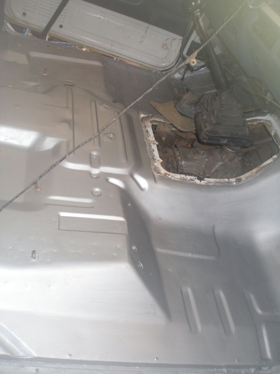 Stripped Ford Bronco interior with silver-painted floor pan and exposed transmission through cut tunnel opening