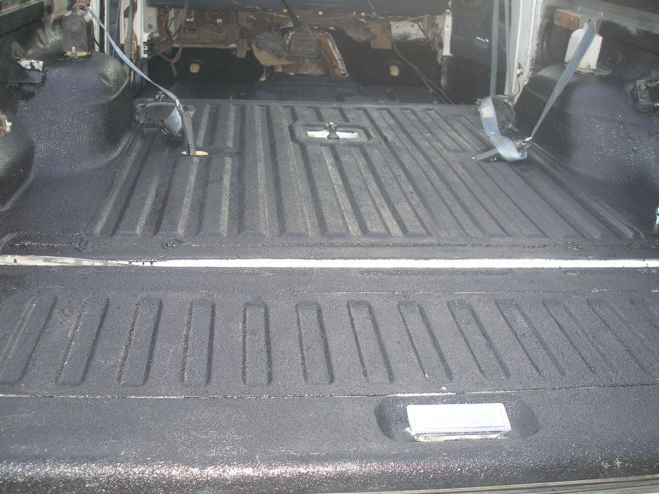 Bronco cargo floor and tailgate coated in black spray-on bedliner, interior stripped with blue seat belts visible