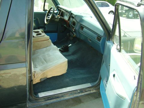 1980 Ford Bronco - The interior of a truck shows a blue dashboard, tan seats, and a manual transmission shifter on the floor.