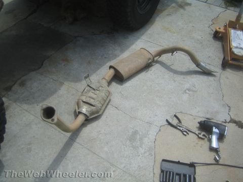 1987 Suzuki Samurai - An exhaust system, including a catalytic converter and muffler, lies on a concrete surface with tools nearby.