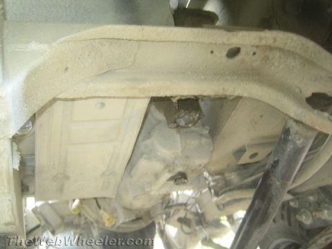 1987 Suzuki Samurai - The undercarriage of a vehicle, focusing on the transmission and frame, appears dusty and shows signs of wear.