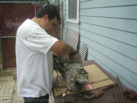 1987 Suzuki Samurai - Man works on a transmission assembly, possibly for a Suzuki Samurai, outdoors.