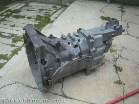 1987 Suzuki Samurai - A metal transmission sits on a cracked concrete surface with some weeds growing through the cracks.