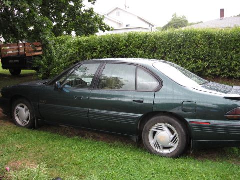 1992 Ford Crown Victoria - This green sedan, likely a 1992 model, is parked on a grassy area next to a hedge.