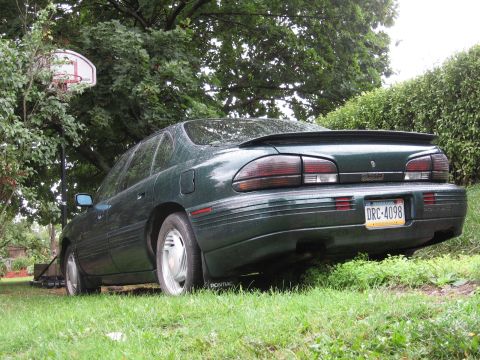 1992 Ford Crown Victoria - This green sedan, viewed from the rear, is parked on a grassy area with a basketball hoop in the background.