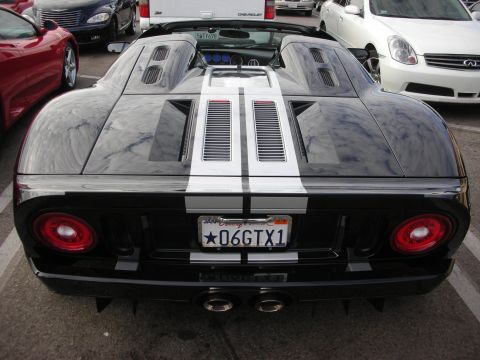 1998 Ford Crown Victoria - A black Ford GT with white racing stripes is parked in a lot, showing its rear end and dual exhaust pipes.