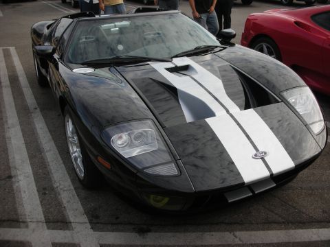 1998 Ford Crown Victoria - Black Ford GT sports car with white racing stripes, parked in a lot next to a red Ferrari.