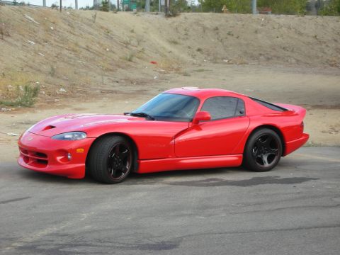 1998 Ford Crown Victoria - A bright red 1996 Dodge Viper RT/10 is parked on asphalt with a dirt embankment in the background.
