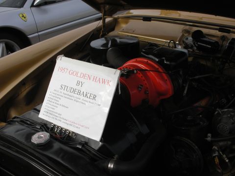 1998 Ford Crown Victoria - The engine compartment of a 1957 Studebaker Golden Hawk is displayed, with a sign providing specifications and contact information for sale.
