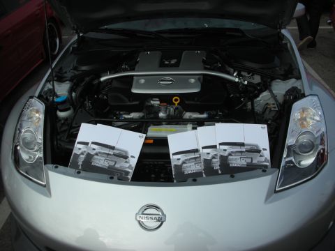 1998 Ford Crown Victoria - Brochures displaying the rear of a Nissan Z car are placed in the engine bay of a silver Nissan Z.