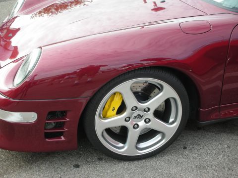 1998 Ford Crown Victoria - Close-up of a red sports car's front wheel and fender, showing yellow brake calipers and RUF wheel branding.