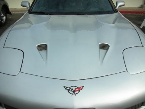 1998 Ford Crown Victoria - Front view of a silver Chevrolet Corvette C5, distinctive hood vents and the iconic crossed flags emblem.