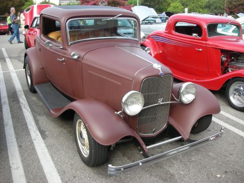 1998 Ford Crown Victoria - A maroon 1932 Ford hot rod coupe is parked next to a red coupe at a car meet.