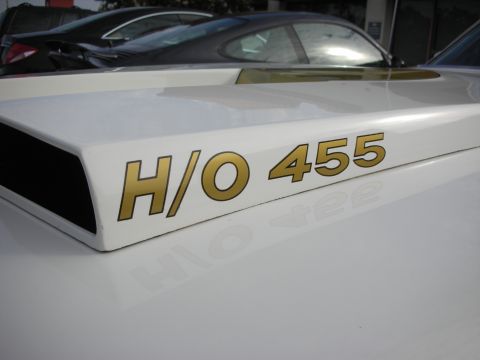 1998 Ford Crown Victoria - Close-up of a white car hood gold 'H/O 455' lettering, with other vehicles visible in the background.