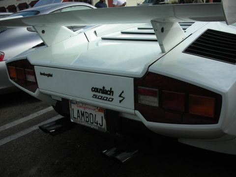 1998 Ford Crown Victoria - The rear of a white Lamborghini Countach 5000 S is visible, a prominent wing and a custom California license plate.