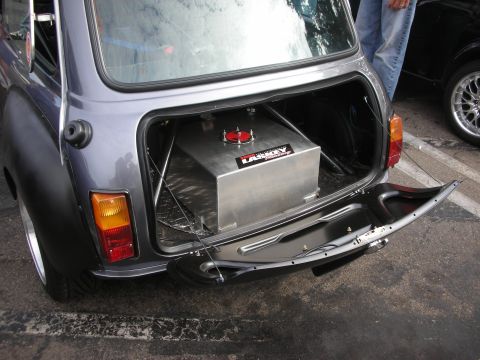 1998 Ford Crown Victoria - A Mini Cooper's rear is shown with its trunk open, displaying a custom fuel cell and a glimpse of another vehicle in the background.