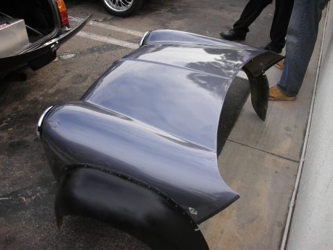 1998 Ford Crown Victoria - A gray hood and fender assembly, likely for a classic car, is displayed on the ground with people standing nearby.
