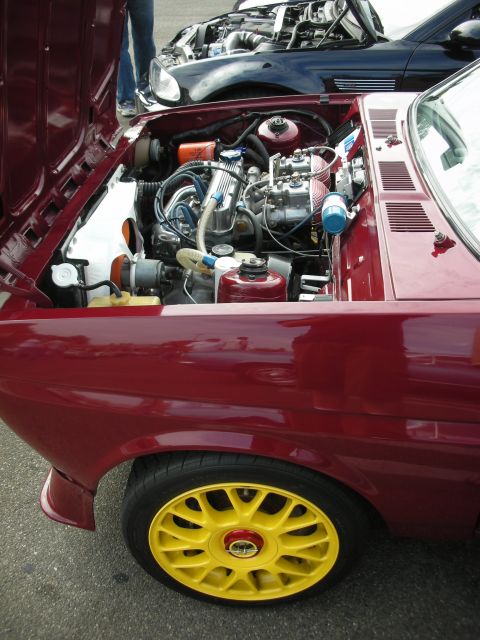 1998 Ford Crown Victoria - The engine bay of a red car is open, revealing its mechanics, with another vehicle visible behind it.