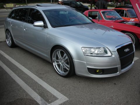 1998 Ford Crown Victoria - A silver Audi wagon is parked at a car meet, with classic red cars visible in the background.