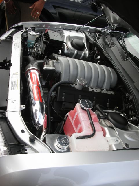 1998 Ford Crown Victoria - The engine bay of a silver car displays a HEMI engine with a chrome intake pipe and red coolant.