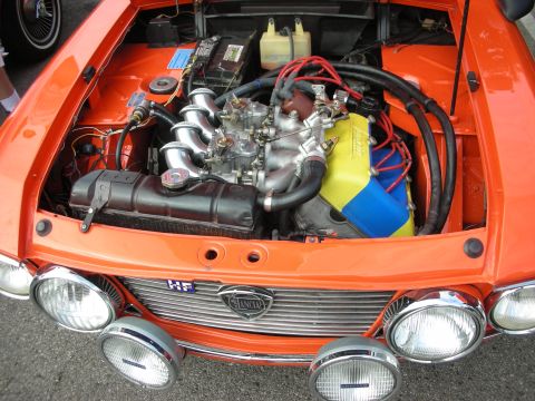 1998 Ford Crown Victoria - The engine bay of an orange Lancia is open, revealing its intricate mechanical components and vibrant wiring.