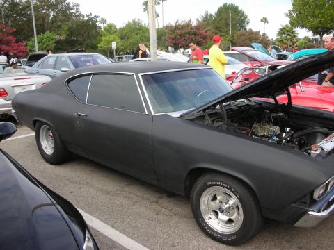 1998 Ford Crown Victoria - A matte black 1969 Chevrolet Chevelle coupe is displayed with its hood open at a car meet.