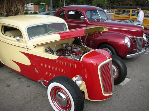 1998 Ford Crown Victoria - A custom hot rod is parked next to a maroon sedan and a wood-paneled station wagon.