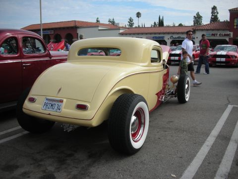 1998 Ford Crown Victoria - A custom yellow hot rod coupe with red flame accents is parked at a car meet, alongside other vehicles.