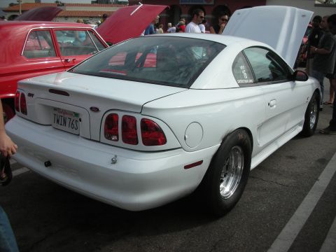 1998 Ford Crown Victoria - A white 1998 Ford Mustang coupe, modified with drag racing tires, is seen at a car meet.