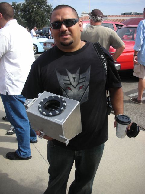 1998 Ford Crown Victoria - A man carries a custom fuel cell at an outdoor car meet with other vehicles visible.