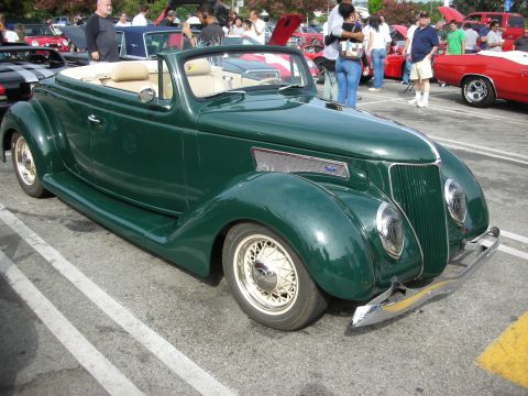 1998 Ford Crown Victoria - A classic green Ford Cabriolet is displayed at an outdoor event with other cars and attendees visible.