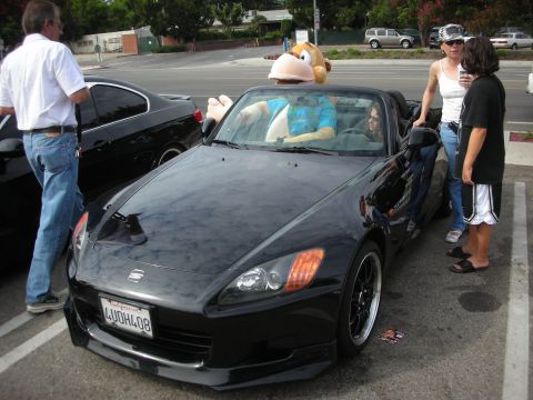 1998 Ford Crown Victoria - A group of people stand around a black convertible with a stuffed monkey visible inside.