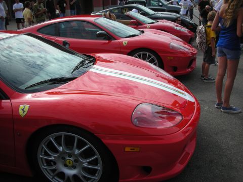 1998 Ford Crown Victoria - Several red Ferrari sports cars are lined up, some with racing stripes, at an outdoor gathering.